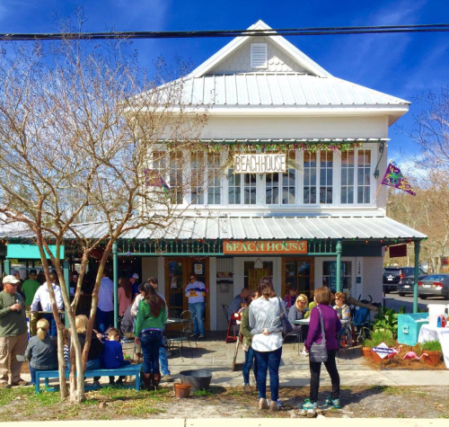 A charming beach house restaurant with a sign, outdoor seating, and people enjoying the sunny day.