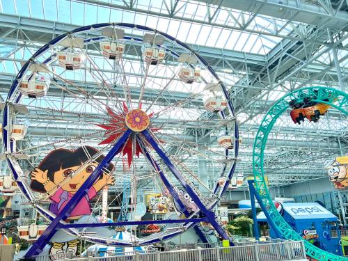 Colorful indoor amusement park featuring a large Ferris wheel and a roller coaster, with cartoon character decorations.