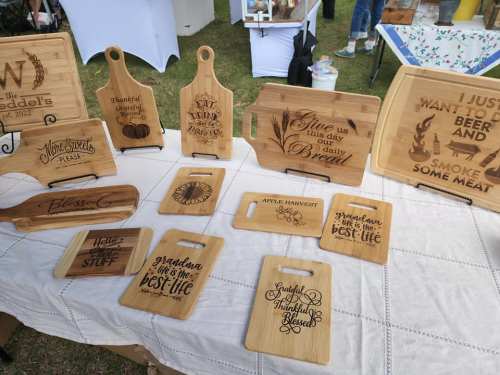 A display of wooden cutting boards and serving trays with various engraved designs and phrases at a market.