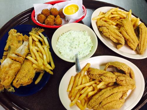 A tray with fried fish, French fries, hushpuppies, and a bowl of coleslaw with a side of dipping sauce.