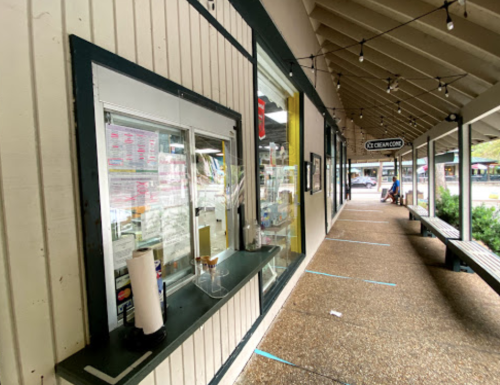 A view of a covered walkway with a service window and benches, featuring string lights overhead.