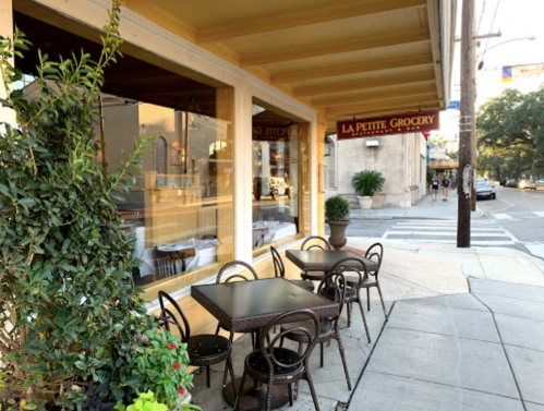 Outdoor seating area of La Petite Grocery, featuring tables and chairs under a yellow awning on a sunny street.