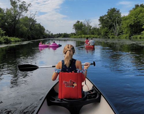 A group of people kayaking and floating on a river surrounded by lush greenery under a blue sky.