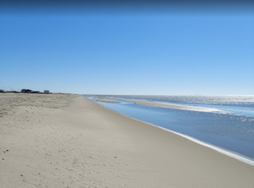 A serene beach scene with soft sand, gentle waves, and a clear blue sky reflecting on the water.