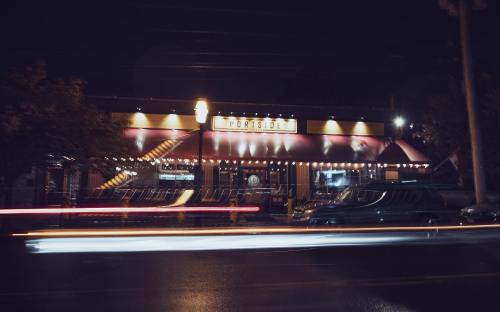 A brightly lit restaurant at night, with string lights and a vibrant exterior, surrounded by moving car lights.
