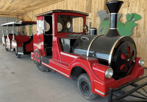 A red and black miniature train with a steam engine design, parked inside a wooden building.