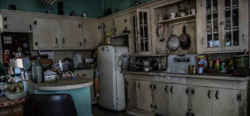A vintage kitchen with worn cabinets, a white fridge, and various dishes scattered on countertops.