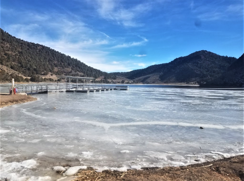 A frozen lake with a dock, surrounded by mountains under a clear blue sky.