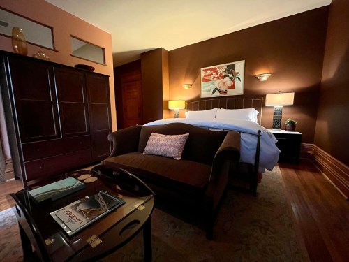 Cozy bedroom with a brown color scheme, featuring a bed, a sofa, and a wooden wardrobe, illuminated by soft lamps.