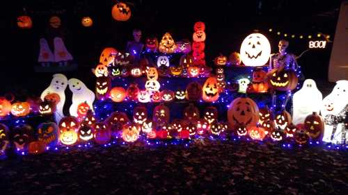 A vibrant Halloween display featuring numerous carved pumpkins, glowing ghosts, and festive lights.