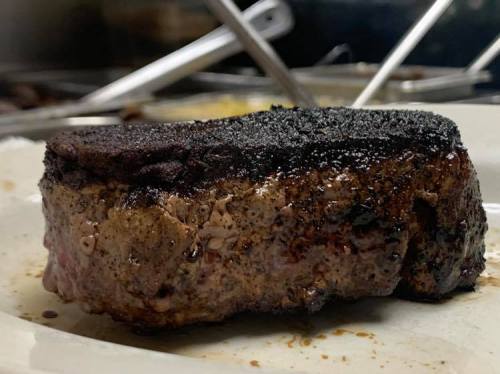 A close-up of a well-cooked steak with a charred exterior, resting on a plate with a glossy sheen.