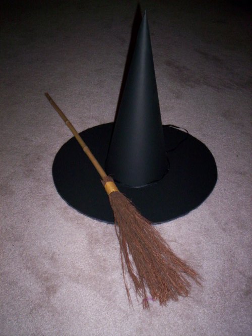 A black witch's hat and a broomstick resting on a light-colored carpet.