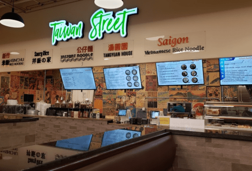 Interior of a food court featuring signs for "Taiwan Street" and "Saigon," with digital menus and a vibrant decor.