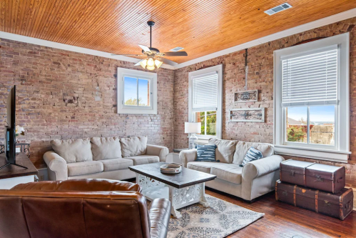 Cozy living room with brick walls, two sofas, a coffee table, and large windows letting in natural light.