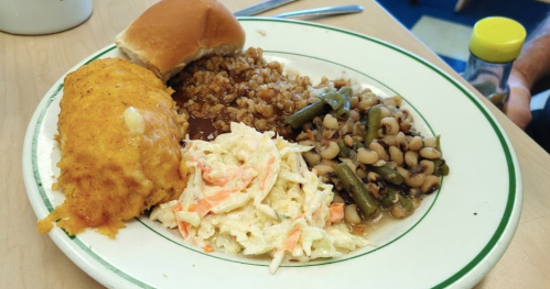 A plate of food featuring cornbread, coleslaw, green beans, black-eyed peas, and a roll.