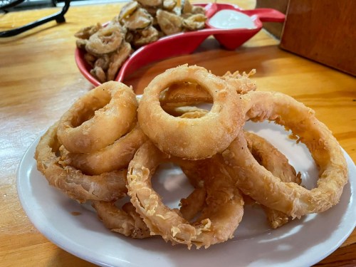 A plate of golden, crispy onion rings with a side of dipping sauce in the background.