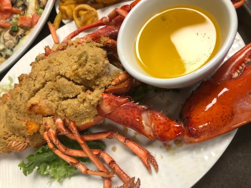 A plate featuring a stuffed lobster with a side of melted butter, garnished with lettuce.