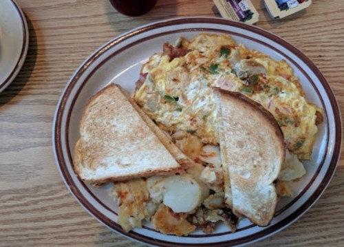 A plate with an omelette, golden toast, and crispy potatoes on a wooden table.