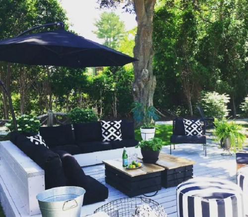 A stylish outdoor seating area with black and white cushions, a wooden table, and greenery under a large umbrella.