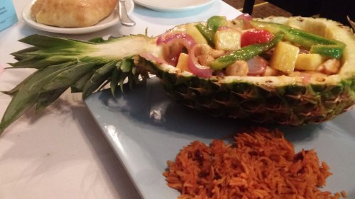 A pineapple half filled with colorful stir-fried vegetables and served with a side of rice on a blue plate.