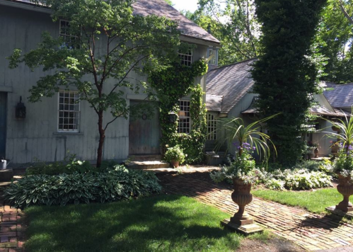 A charming house surrounded by lush greenery and flower beds, featuring stone pathways and decorative planters.