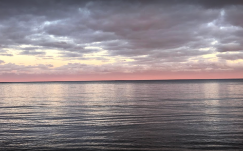 A serene seascape at sunset, with calm waters reflecting soft pink and gray clouds in the sky.