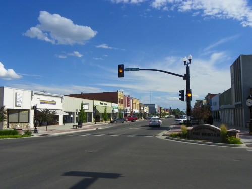 A street view of a small town with shops, traffic lights, and a sign for Fort Morgan under a blue sky with clouds.