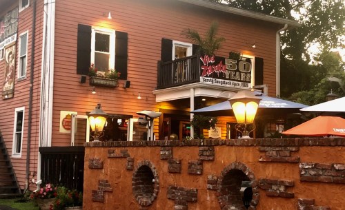 A charming pink restaurant with a balcony, outdoor seating, and a sign celebrating 50 years in business.