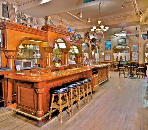 A warm, wooden bar interior with stools, ornate decor, and a spacious seating area in a cozy pub setting.