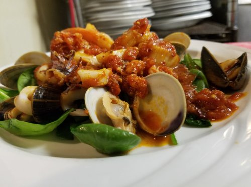A plate of seafood pasta with clams, shrimp, and a rich tomato sauce, served on a bed of fresh spinach.