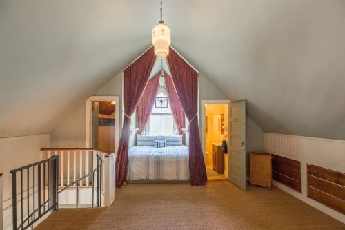Cozy attic bedroom with a sloped ceiling, large window, and elegant curtains, featuring a bed and wooden storage.