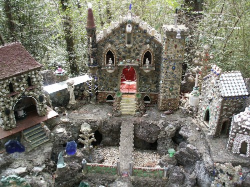 A whimsical miniature village made of stones and colorful decorations, surrounded by trees in a natural setting.