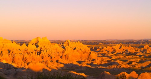 Golden-hued rock formations at sunset in a vast, rugged landscape.