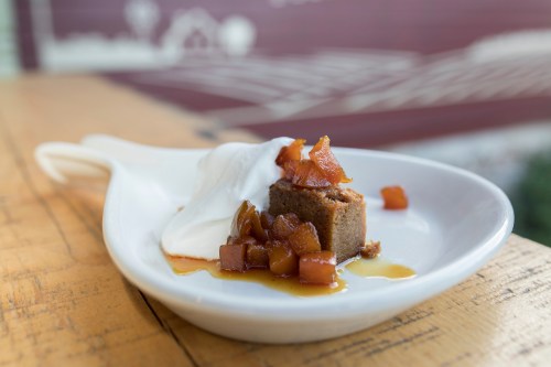 A slice of spiced cake topped with caramelized apples and a dollop of cream on a white plate.
