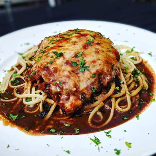 A plate of spaghetti topped with a cheesy meat sauce and garnished with parsley.