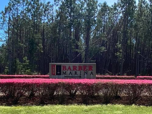 Sign for Barber Marina surrounded by vibrant pink flowers and tall trees in the background.