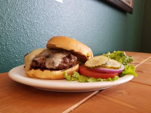 A juicy burger with melted cheese, served on a plate with lettuce, tomato, and pickles, against a green wall.