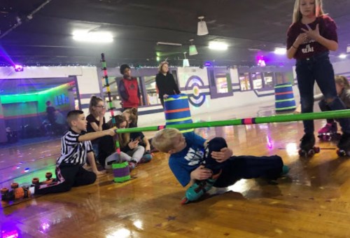 A group of children roller skating, with one boy leaning to pass under a limbo stick while others cheer him on.