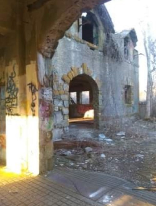 Abandoned building with crumbling walls, graffiti, and overgrown vegetation, illuminated by soft sunlight.