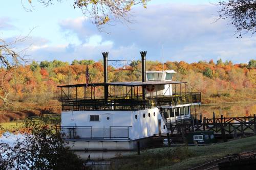 A white boat docked by a river, surrounded by vibrant autumn foliage and a clear blue sky.