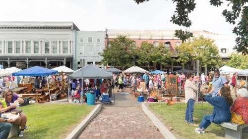 A bustling outdoor market with tents, vendors, and crowds enjoying the day in a lively urban setting.
