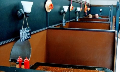 Interior of a diner with brown booths, wall sconces, and condiments on a table, creating a cozy atmosphere.