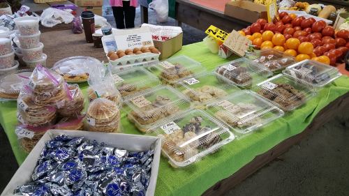 A market table displaying various baked goods, including cookies and pastries, alongside fresh produce.