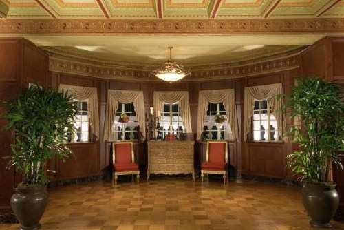 Elegant interior with wooden walls, large windows, potted plants, and two red chairs in a well-lit room.