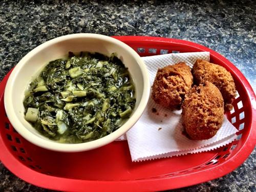 A red tray holds a bowl of cooked greens and three golden-brown cornbread fritters on a napkin.