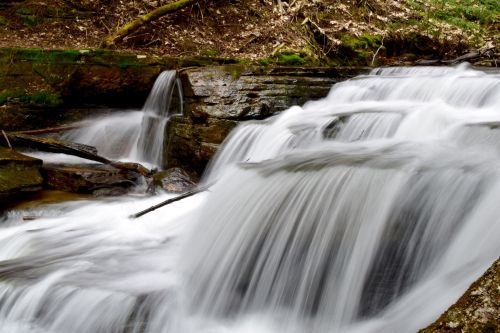 A serene waterfall cascading over rocks, surrounded by lush greenery and natural scenery.