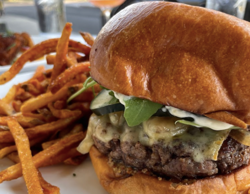 A juicy cheeseburger with lettuce, pickles, and sauce, served with crispy sweet potato fries on the side.
