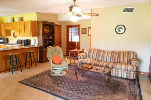 Cozy living room with a striped sofa, coffee table, and a ceiling fan, leading to a kitchen and front door.