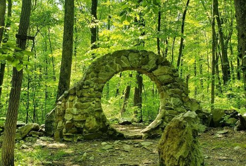 A stone archway surrounded by lush green trees in a serene forest setting.