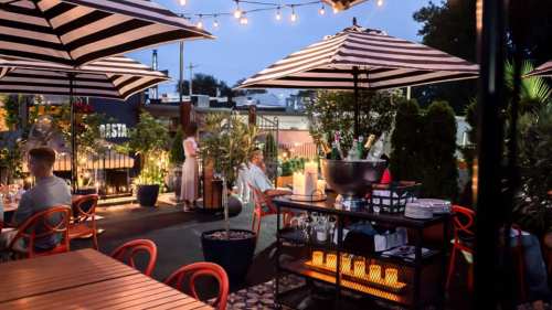 A stylish outdoor dining area with striped umbrellas, plants, and soft lighting, creating a cozy evening atmosphere.